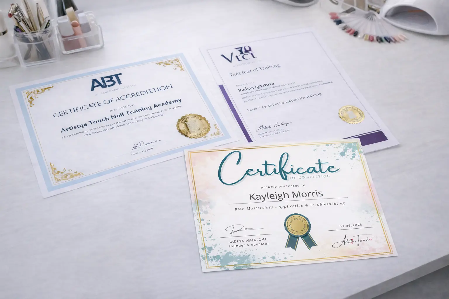 ABT and VTCT accreditation certificates displayed on desk with nail training materials
